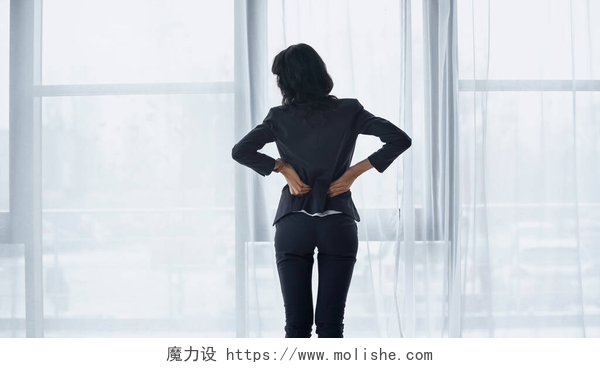 一个站在窗户前的女人背影女商人站在办公室窗边时背痛的后视镜 